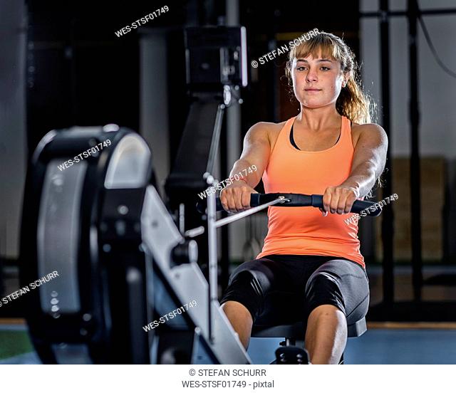 Athletic young woman exercising with rowing machine at gym