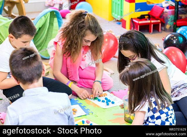 Group of kids applying colorful plasticine on various drawings printed on paper sheets during educational activity in the classroom of a modern kindergarten