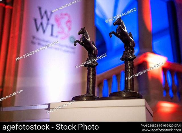 28 August 2021, North Rhine-Westphalia, Münster: Two trophies of the Westphalian Peace Award stand on a pedestal in front of the logo of the Economic Society of...