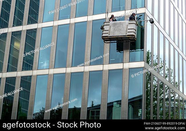 07 June 2021, Bavaria, Munich: Two men in a crane basket clean the windows and the facade of a modern high-rise building. Photo: Peter Kneffel/dpa