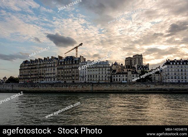 france, paris, dramatic clouds over notre dame at sunset, apartment buildings on the seine