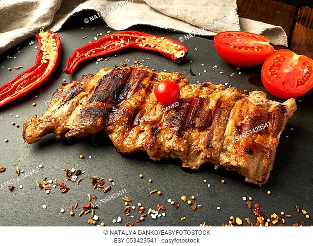 grilled pork ribs on a black board, fresh red tomatoes and chili peppers, top view