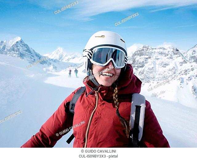 Young woman skier wearing helmet and ski goggles smiling in snow covered landscape, portrait, Alpe Ciamporino, Piemonte, Italy