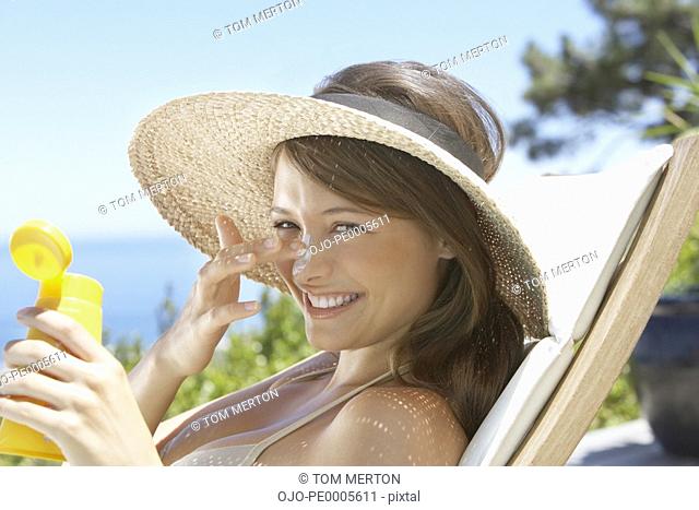 Woman with straw hat applying sunblock to face outdoors