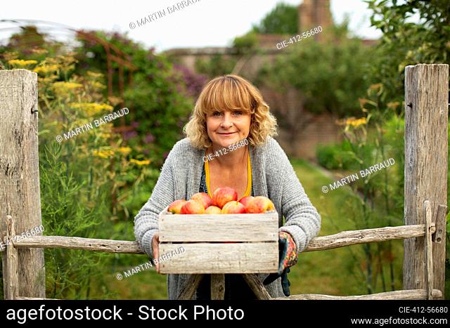 Portrait happy woman with crate of fresh harvested apples in garden