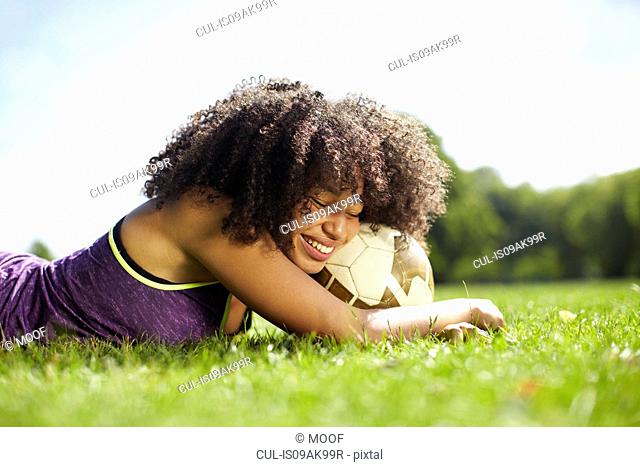Young woman taking a break in park leaning on football