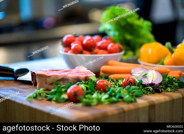 Juicy slice of raw steak with vegetables around on a wooden table