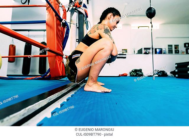 Female boxer squatting by boxing ring ropes