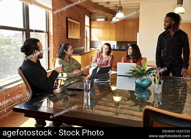 group of co-workers sitting at large conference table with their devices having discussion