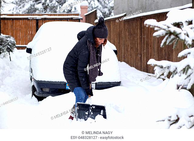 woman with shovel cleaning snow aeound car. Winter shoveling. Removing snow after blizzard