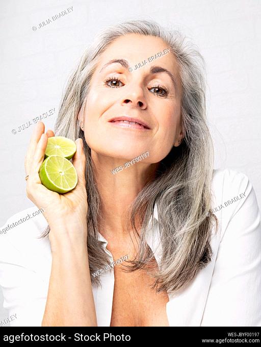 Smiling mature woman holding lemon in front of wall
