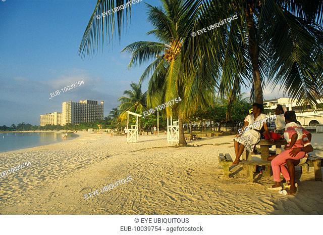 Mallard beach with people sitting beneath palm tree in foreground and hotel beyond