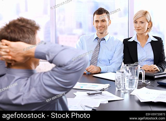 Professionals sitting at at meeting table in skyscraper office, smiling, looking at executive