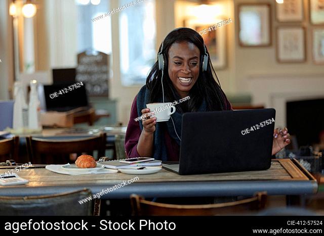 Woman with headphones drinking coffee and working at laptop in cafe