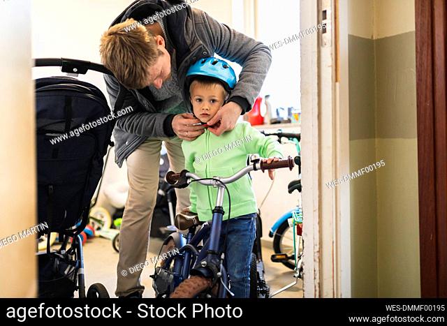 Father wearing cycling helmet to son at home