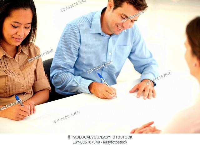 Portrait of male and female worker signing a contract while smiling and sitting on office desk