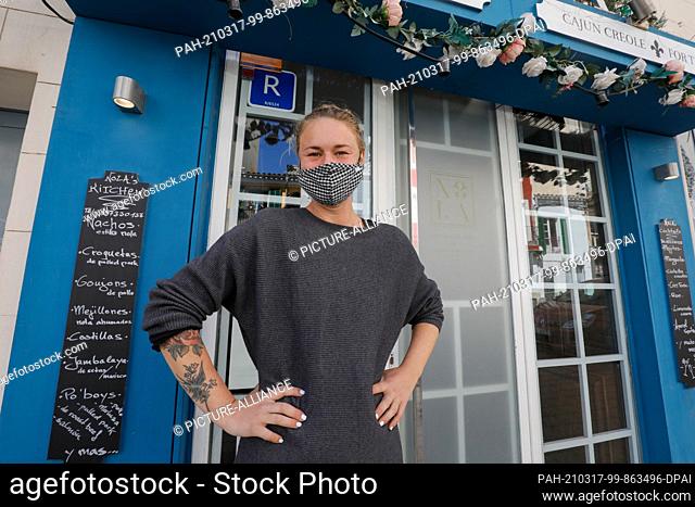 17 March 2021, Spain, Palma: Nadia, owner of Nola restaurant, smiles behind her mouth-nose covering in front of the restaurant
