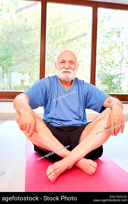 Vitaler Senior Mann sitzt entspannt auf eine Yoga Matte im Fitnesscenter