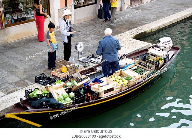 A fruit and vegetable vendor serving a customer from his boat moored alongside the Fondamenta dei Vetrai along the Rio dei Vetrai canal on the lagoon island of...