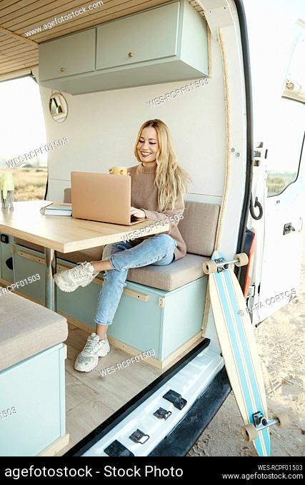 Happy digital nomad working on laptop sitting inside motor home