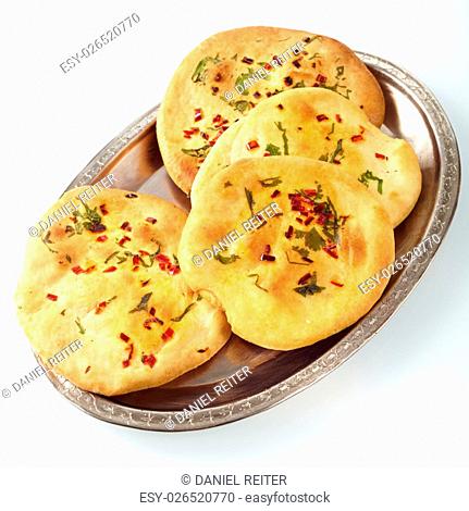 Silver plate of four circular naan bread patties garnished with red and green tasy herbs on white surface