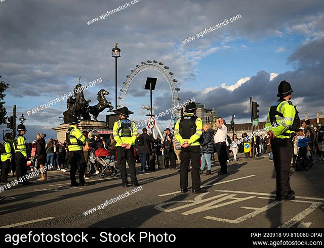 18 September 2022, Great Britain, London: Police officers stand on Westminster Bridge near Westminster Hall along with passersby queuing to say farewell to...