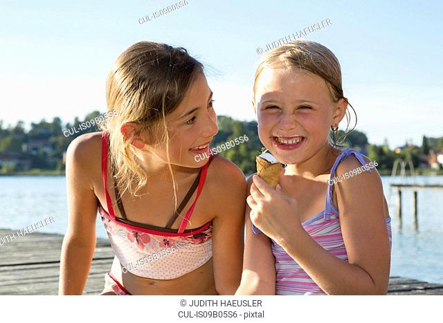 Two sisters on pier eating ice cream cones, Lake Seeoner See, Bavaria, Germany