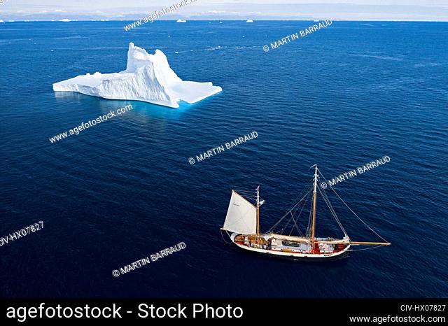 Ship sailing past majestic iceberg on sunny blue Atlantic Ocean Greenland