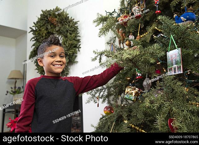 Young boy smiling at camera while decorating Christmas tree