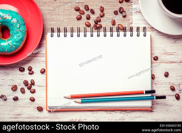 Opened notepad and cup of coffee with donut on wooden table
