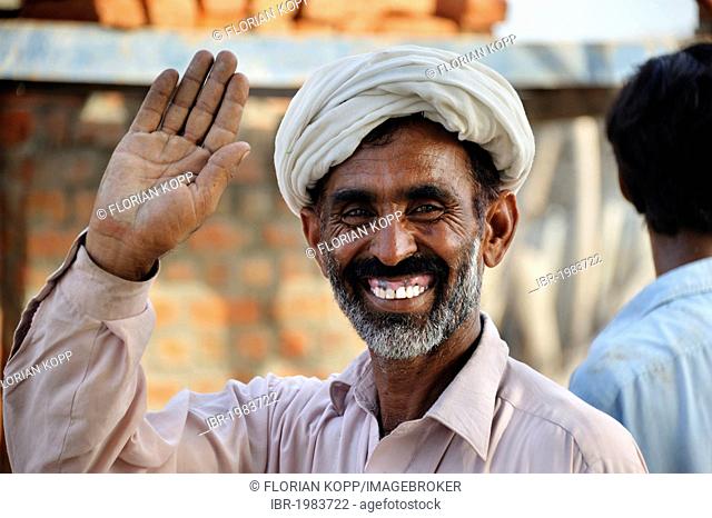 Smiling man with a turban lifting hand in greeting, Lashari Wala village, Punjab, Pakistan, Asia