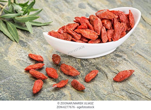 a bowl of dried Tibetan goji berries (wolfberry) with a fresh goji leaf on a slate rock surface