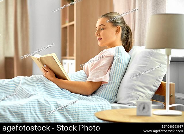 smiling girl reading book in bed at home