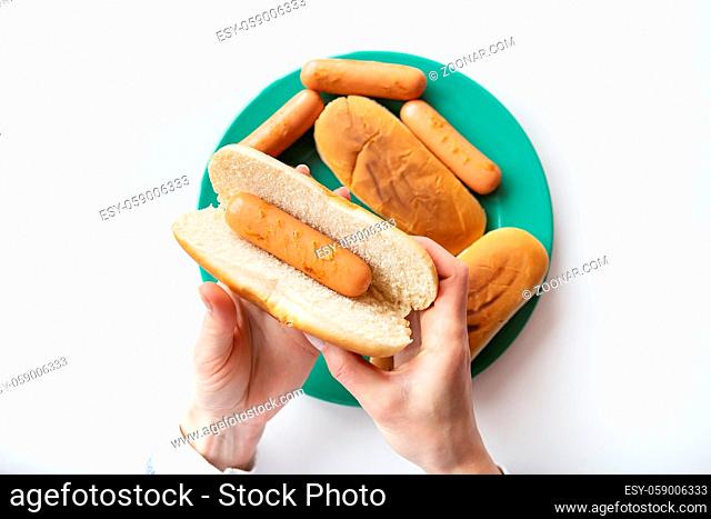 Fresh buns for making hot dogs that lie on a green plate along with sausages that the girl holds in her hands. Top view, close-up