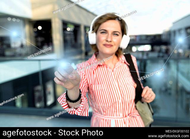 Smiling woman listening music through wireless headphones touching graph in shopping mall