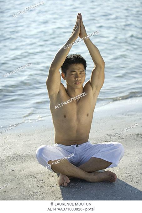 Man sitting on beach in yoga prayer position