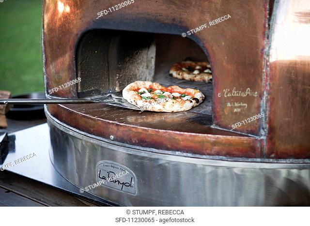A margherita pizza being taken out of the wood-fired oven