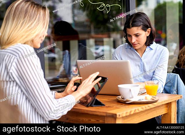 Medium-shot of two female diverse co-workers focused on their work in outdoors office