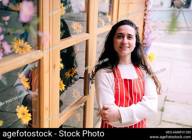 Smiling florist wearing apron standing with arms crossed