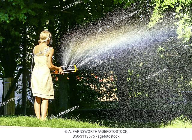 A woman waters the grass with a hose in the Hagalund Park and apartment complex, Solna suburb. Stockholm, Sweden