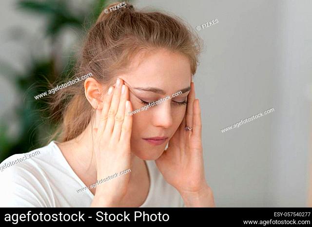 Young fatigued woman having strong headache suffering from chronic migraine or blood pressure hypertension massaging temples to relieve head ache pain