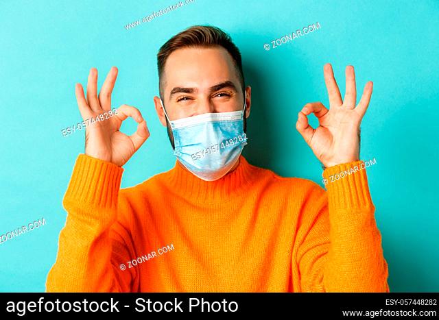 Covid-19, social distancing and quarantine concept. Close-up of satisfied male model in medical mask showing okay signs, praising and agreeing