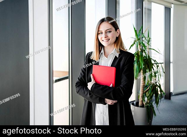 Happy beautiful businesswoman holding tablet PC near window in office