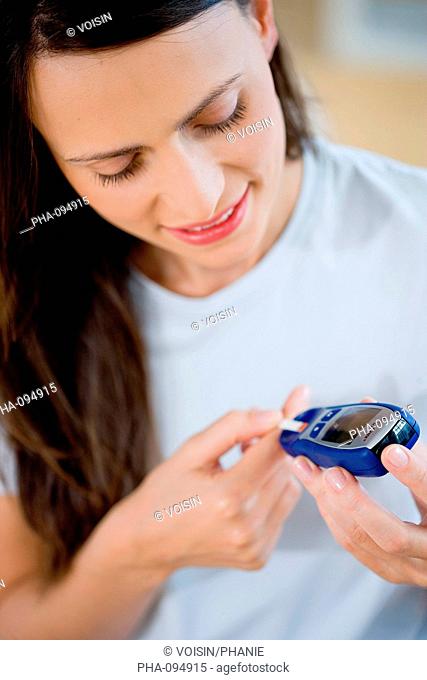 A diabetic person is checking her blood sugar level self glycemia. A drop of blood obtained with a pen-like lancing device is placed on a test stick and...