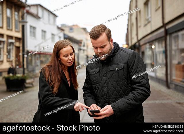 Man and woman standing in street and checking phone