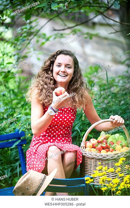 Smiling young woman with with wire basket of different fruits in a garden
