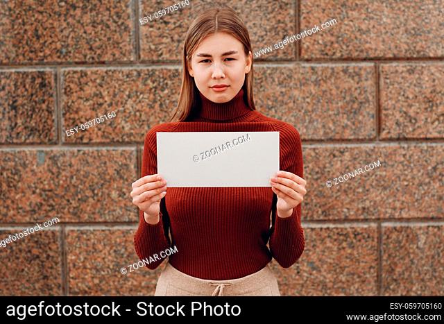 Girl holds white paper in hand stone background. Young woman with white blank template sheet with empty space