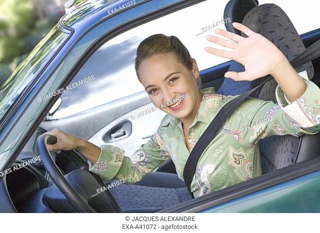 Happy young woman waving from a car