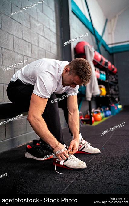 Young male athlete tying shoelace in gym