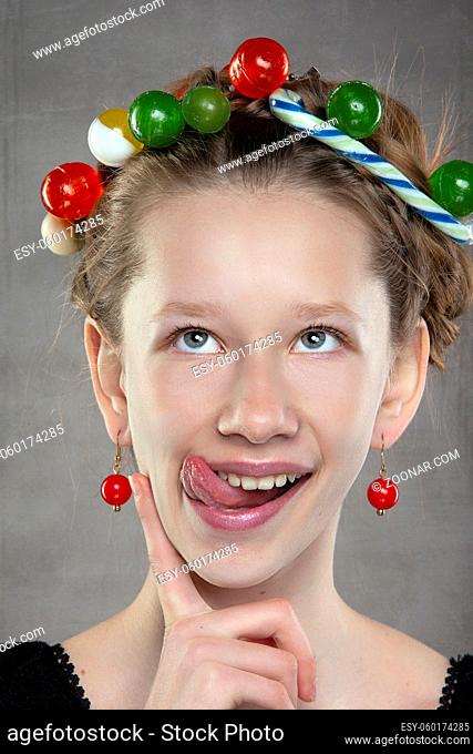 A funny teenager girl with a wreath of sweets on her head shows her tongue